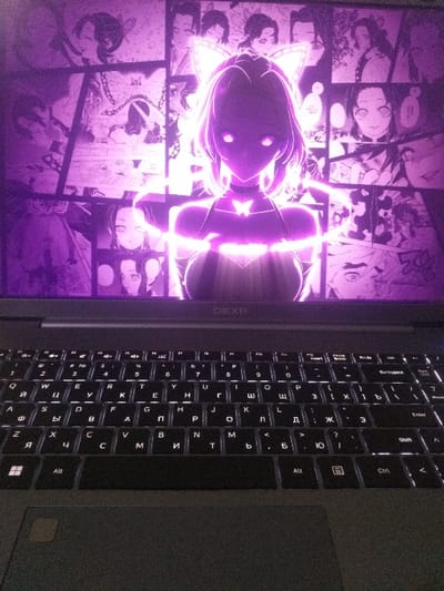 A laptop displays a vibrant, manga-style image with a glowing, neon-purple anime character. The background showcases various manga panels. The keyboard is visible on the right, with illuminated keys showing Cyrillic and Latin characters. The laptop brand, "DEXP," is printed vertically on the side of the screen. The overall lighting is dim, highlighting the laptop's screen and keyboard.