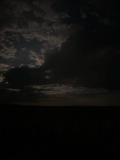 The image shows a dark, partially cloudy night scene. The left portion of the image is filled with scattered clouds, faintly illuminated. The right portion is completely dark, obscuring details. The image is not clear enough to determine the location or any actions, subjects, or interactions.