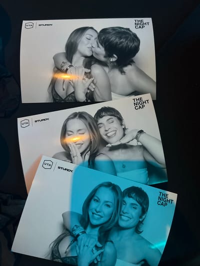 The image shows three identical promo flyers for a business named "The Night Cap" lying on a dark surface, possibly a table or floor. Each flyer has the logo and name of "The Night Cap" at the top, with the branding "UTA" and "STURDY." near the bottom left. The flyers feature black-and-white portrait of two female models in an intimate embrace, with varying blue tone washes over the photographs. The photographs are likely promotional material for a brand or event in the city of Indian Wells, United States of America.