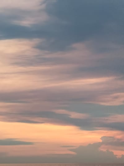 The image is a close-up vertical shot of a sky filled with clouds. The clouds display a gradient of colors, transitioning from a soft pink and orange near the bottom to blues and grays at the top. The lighting suggests either sunrise or sunset. No people, subjects, or objects are visible beyond the sky itself. The scene is entirely composed of atmospheric elements. The location provided, Prijevorac, Montenegro, cannot be verified from the visual information in the image.