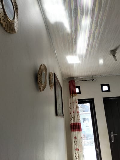 A side view shows a white wall with three circular gold-framed mirrors and a framed picture hanging on it. A curtain with red floral patterns is to the right of the wall, partially covering a window with a black frame. A closed black door is visible in the right corner, and two square windows are positioned above it. The ceiling has a patterned design.