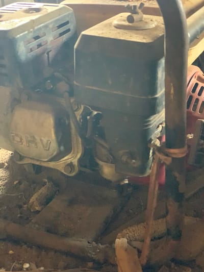 The image shows a close-up of the engine of a small, gas-powered machine. The engine is mostly obscured by dirt and rust, with some of the metal parts visible. The engine is located in Egbeda, Nigeria, at the coordinates 7.12 latitude and 5.362 longitude. The image suggests that the machine is in a state of disrepair. It is difficult to say anything further about the scene, as the image provides only a limited view.
