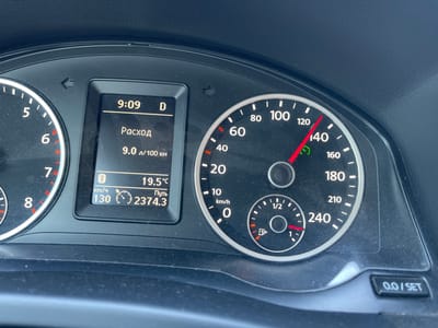 The image shows a close-up of a car's dashboard. The dashboard displays a digital clock showing 9:09, the gear selector is in "D" (Drive), and the fuel consumption is 9.0 liters per 100 kilometers. The outside temperature is 19.5 degrees Celsius. The odometer shows 2374.3 kilometers traveled. The speedometer indicates the car is traveling at 130 km/h. A fuel gauge shows the fuel level is slightly above the "1" mark. The image is taken from inside the car, looking at the instruments. The environment appears to be daytime, with natural light reflecting off the dashboard. There is no visible indication of the location being Hrozyne, Ukraine.