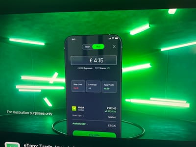 A smartphone is displayed in a dark, ambient environment with bright green lighting and neon tubes. The phone screen shows a trading application interface. The application displays information about NVIDIA (NVDA) stock, including current price, exposure, shares, and order details. The user appears to be considering a purchase, with options for "Stop Loss," "Leverage," and "Take Profit" visible. A "Buy NVDA" button is prominently displayed at the bottom of the screen. Text overlays on the image state, "For illustration purposes only" and partially visible text at the bottom mentions "eToro: Trade, Invest...". The overall aesthetic suggests a modern, tech-focused presentation. There is no discernible location within the city of Cheltenham, United Kingdom, indicated in the image.