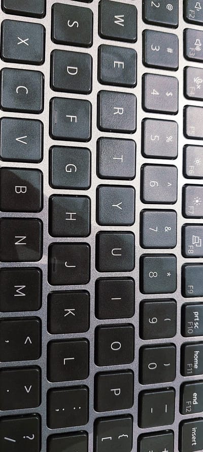 A close-up, vertical shot of a laptop keyboard shows rows of black keys with white lettering. The keys are arranged in a standard QWERTY layout, with some keys featuring additional symbols. The keyboard appears to be part of a modern laptop with a metallic frame. The lighting is even, highlighting the texture of the keys and the slight sheen on their surface. The overall impression is one of a functional and clean electronic device. There is no visible indication of the location in Pagedangan, Indonesia.