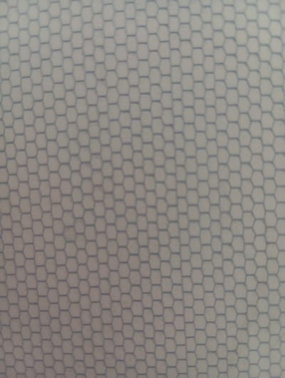 The image is a close-up, slightly out-of-focus shot of a textured surface with a repeating hexagonal pattern. The pattern consists of thin, dark blue lines forming interconnected hexagons against a lighter, possibly off-white or very pale gray background. The texture appears uniform across the entire frame. There are no people, objects, actions, interactions, or environmental elements present that would indicate a specific location within the city of Hlynytsi, Ukraine, or any other city. The image solely captures a repeating geometric pattern.