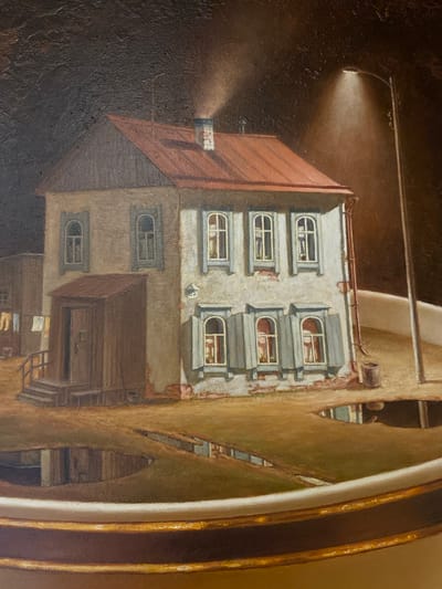 This painting depicts a nighttime street scene in a European-style town. A lone streetlamp casts a soft glow on a building with a red roof and multiple windows. The building appears to be old, with some signs of wear and tear. The windows are arched and have shutters, and some appear to have curtains or blinds. There is a doorway on the lower level, with a set of stairs leading up to it. Laundry is hanging on a line outside the building, suggesting that people live there. The overall mood of the painting is quiet and somewhat melancholic, with the dark, textured background and the solitary light contributing to a sense of isolation. The painting is framed by a decorative border. The scene appears to be in a town setting, possibly in Russia given the location context, though the architectural style suggests a European influence. The time of day is clearly night, indicated by the streetlamp and the dark sky. There is no visible text in the image.