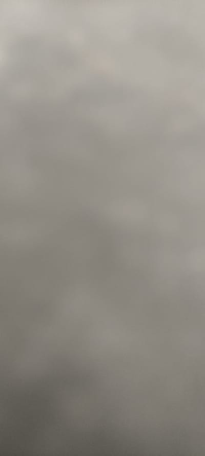 The image is a slightly out-of-focus, neutral-toned photograph of a cloudy sky. There are no discernable objects, people, or specific environmental features visible. The texture suggests a soft, diffused light, indicative of an overcast day. The image lacks any contextual clues related to a specific location, including Andijan City, Uzbekistan.