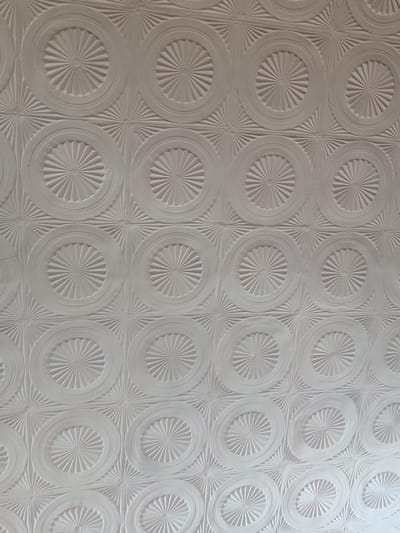The image is a close-up, full-frame shot of a white, textured ceiling with a repeating pattern of raised concentric circles. Each circle contains a starburst design with radiating lines. The pattern is uniform and covers the entire visible area. The lighting appears to be soft and diffused, creating subtle shadows that highlight the relief of the pattern. There are no people, objects, or specific environmental features visible beyond the textured ceiling. The location in Otaci, Moldova, is not discernible from the image itself.