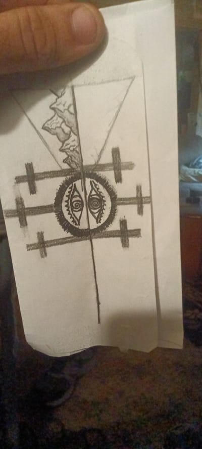 A hand holds a piece of paper with a pencil sketch on it. The drawing includes a triangle at the top, below that is a gear-like circle with two eye-shaped figures inside it. Horizontal lines with crosses attached to each end surround the circle. A single line extends down from the circle. The background is blurry and indistinct but appears to include furniture and a plant. The location is Clarksville, United States.