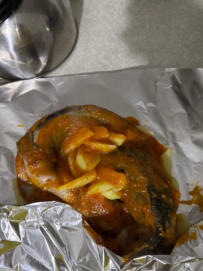The image shows a cooked fish dish, likely salmon, coated in a tomato-based sauce with sliced potatoes, and resting on aluminum foil. A metal bowl is partially visible to the left of the foil. The location of the image is not discernible from the visual information provided. The city of Rotherham, United Kingdom is not discernible from the image.