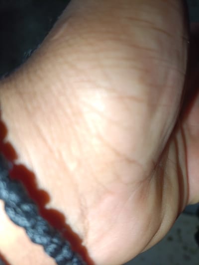 This extreme close-up photograph features human skin, likely from a hand or foot, alongside a black braided cord. The skin occupies most of the frame, displaying its natural contours, fine lines, and folds. Its complexion appears light to medium, with warm, rosy undertones. A prominent black braided cord, possibly a bracelet or anklet, runs diagonally across the lower left side of the image, creating a distinct shadow on the skin.
The lighting is uneven, with a bright, soft highlight illuminating the central and upper right portions of the skin, suggesting a light source from that direction. This creates a contrast with the shadowed areas and the background. The background is dark and completely out of focus, offering no specific environmental cues. No specific activity is taking place; the image is a static, detailed shot. There is no visible text. The photograph provides an intimate and abstract view of these textures, taken in Polis Chrysochous, Cyprus.
