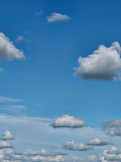 The image displays a bright blue sky with scattered white and grey clouds of various sizes and densities. Some clouds are wispy and thin, while others are more voluminous and textured, indicating different atmospheric conditions. The lighting suggests it is daytime, likely with the sun above and slightly to the side, casting shadows on the denser clouds. The photograph appears to be taken from an outdoor location, looking upwards at the sky. The provided information does not mention Gargždai, Lithuania, or any specific location within the city. There are no people, subjects, objects, or actions depicted in the image; it is solely a natural landscape scene of the sky.