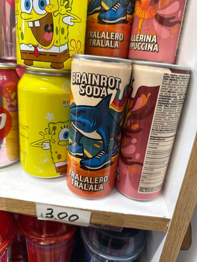 This is a close-up, eye-level shot of several colorful soda cans arranged in a retail display. The cans feature vibrant cartoon characters and playful lettering. One can prominently displays a stylized illustration of Spongebob Squarepants, while another has a shark character with the text "BRAINROT SODA." A pink can has a character that resembles a ballerina with the text "LLERINA PUCCINA." The cans are stacked and appear to be part of a larger selection. A price tag with "3.00" is affixed to the shelf in the foreground. The background shows additional cans and a blurred view of shelves and possibly other products. The overall impression is of a brightly lit, well-stocked retail environment, likely a convenience store or supermarket aisle. The text on the cans is in multiple languages and includes nutritional information and ingredients, suggesting a European origin. The Spongebob cans also have Chinese characters. The scene is static, focusing solely on the product display.