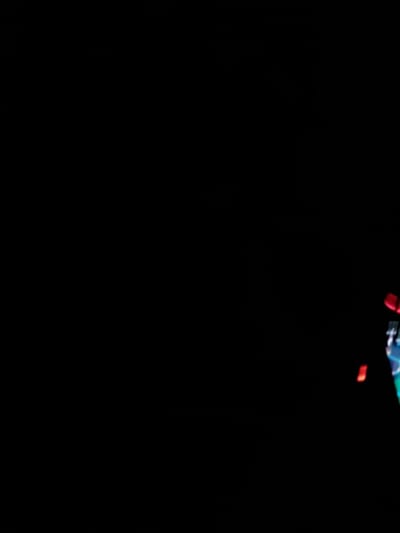 The image shows a predominantly dark, nearly black background. Near the top right corner, there are indistinct, blurred elements suggesting the presence of objects or shapes, possibly involving teal, blue, and red colors. The details are insufficient to clearly identify the objects or their characteristics. The image is dominated by the dark background with a small area of obscured color at the top.