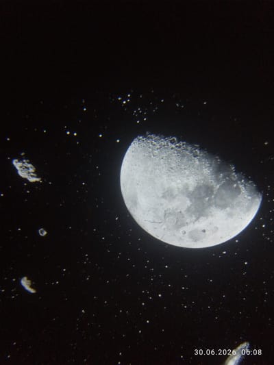 The image is a close-up, low-angle photograph of the moon against a dark, starry sky. The moon is partially illuminated, showing craters and surface details. There are also several small, irregularly shaped objects in the foreground, appearing to be debris or possibly other celestial bodies. A timestamp in the bottom right corner reads "30.06.2026 06:08". The context provided about TashGRES, Uzbekistan, is not visually represented in the image itself.