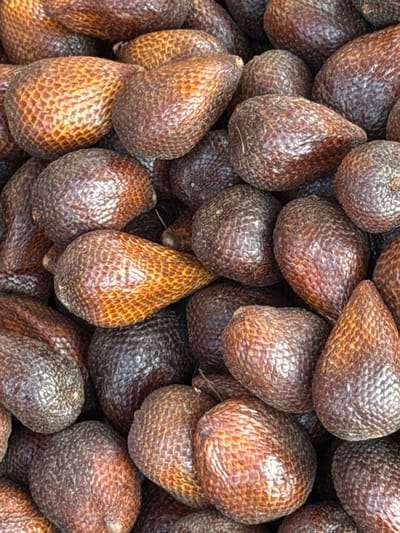 A close-up, top-down view of a pile of salak fruits, commonly known as snake fruit, is presented. The fruits are ovoid in shape with a rough, scaled skin that ranges in color from dark reddish-brown to a lighter coppery-brown. The scales create a textured pattern across each fruit. They are densely packed together, filling the entire frame of the image. No people are visible, and the background is entirely occupied by the salak fruits. The lighting appears to be natural, highlighting the contours and textures of the fruit. The image does not provide any specific location information within Karangsambung, Indonesia, beyond the general context.