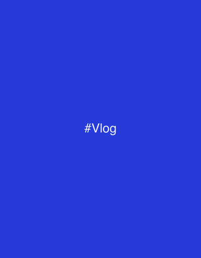 The image displays a uniform, solid royal blue background. Centered horizontally and vertically on this blue field is the white text "#Vlog" in a sans-serif typeface. No other visual elements, such as people, specific objects, detailed subjects, actions, interactions, or an identifiable environment within Kalyvia Thorikou Municipal Unit, Greece, are present or discernible in the frame. The scene is static and purely textual against a monochrome background.