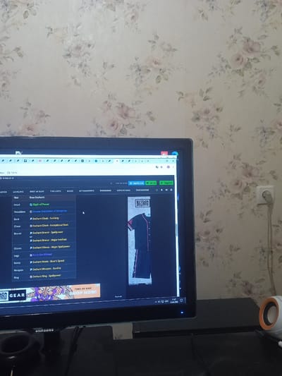 The image shows a computer monitor displaying a website related to the game Diablo IV. The website appears to be a guide or database, listing enchantments for various gear slots such as Head, Shoulders, Back, Chest, Bracer, Gloves, Legs, Boots, Weapon, and Ring. The screen also shows a Blizzard logo and an advertisement for pins. The monitor is positioned on a desk, with a Samsung logo visible on a device below it. The background is a floral wallpaper. A wall socket with a plug is visible on the right side of the image. The time displayed on the computer's taskbar is 11:47 on 15.05.2025. The image does not contain any information about the location being Karnaukhivka, Ukraine.