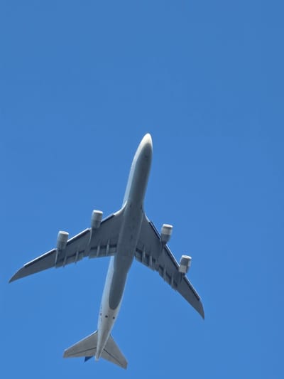 An underside view of a large, white passenger airplane against a clear blue sky is captured from below. The airplane is angled upwards, with its wings extended and its engines clearly visible beneath them. The tail section of the plane, including the horizontal and vertical stabilizers, is also visible. The image does not provide any specific details that would indicate its location in Bischofsheim, Germany.
