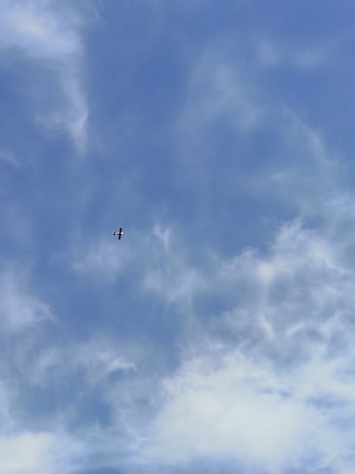 A small airplane is visible in a partly cloudy, blue sky. The location is specified to be Kushnarenkovo, Russia, but the image itself does not confirm this location. No people are visible. The primary object is the airplane, positioned roughly in the center of the frame. There is no action visible other than the implied flight of the plane. The environment consists of the sky and the clouds.