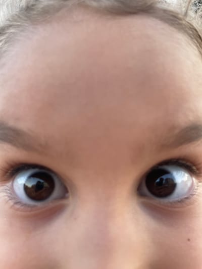 The image is a close-up, low-angle shot of a person's eyes and forehead, with some of their hair visible at the top. The eyes are wide open and appear to be brown. The skin is light-toned and smooth. The image is slightly out of focus. There are no discernible features of the city of Sagunto, Spain, or any specific environment other than a close-up view of a human face.