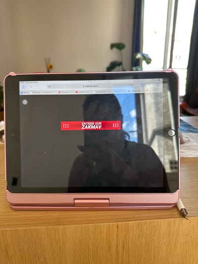 A pink iPad is on a wooden surface. The screen displays a web browser window navigated to the website "zakmav.com". An overlay in the center of the screen reads "ENTRER SUR ZAKMAV". The iPad is next to a white stylus. A window with a glimpse of the outdoors is partially visible in the background. The location is Saint-Ouen-sur-Seine, France.