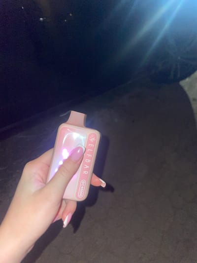 A person's hand with manicured nails holds a pink electronic cigarette device. The device has "ELFBAR" and "BC4500" printed on its side. The background is dark and out of focus, suggesting an outdoor nighttime setting. There is no visible context within the city of Velykyi Buialyk, Ukraine.