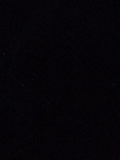 The image is a black and white photograph with a dark, grainy texture. There are three small, faint points of light visible in the image. One is in the upper left quadrant, a second is in the lower left quadrant, and the third is in the middle right quadrant. The image does not provide enough detail to identify any specific location or objects. Therefore, it is not possible to determine the location in Kyzyl-Kyya, Kyrgyzstan.