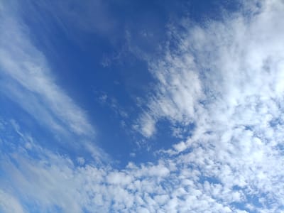 The image displays a clear blue sky with scattered white clouds. The clouds vary in size and density, with some appearing wispy and streak-like, particularly on the left side of the frame, while others are more defined and puffy, especially on the right. The overall scene is characteristic of fair weather. There are no people, subjects, objects, actions, or interactions visible in the image, as it solely captures the sky. The location is identified as Kyzyl Suu, Kyrgyzstan, suggesting a natural outdoor environment.