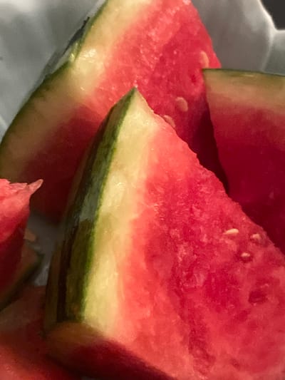 This media file is a close-up, macro shot of several slices of watermelon. The focus is on the vibrant red flesh of the fruit, interspersed with small, pale seeds. The rind of the watermelon is visible, showing a transition from the yellow inner part to a dark green outer layer. The lighting is soft, creating a slightly diffused and warm atmosphere. The composition is tight, emphasizing the texture and juicy appearance of the watermelon. There are no people, text, or discernible location cues within the frame, making it a simple still life of food. The setting appears to be indoors, with a blurred background that suggests a domestic environment. The image conveys a sense of freshness and ripeness.