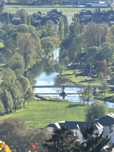 The image presents an aerial view of the Sauer river as it passes through the city of Diekirch, Luxembourg. The river, reflecting the sky, meanders through a green landscape characterized by grassy areas and trees. Along the riverbank, buildings are visible, suggesting the presence of residential or commercial properties. The image captures a peaceful scene with the natural elements of the river and vegetation blending with the built environment of the city.