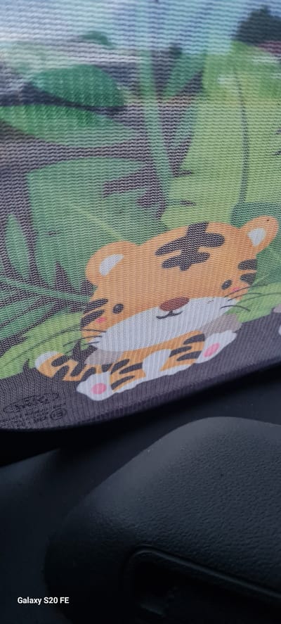 The image displays a close-up view of a car window sunshade featuring a cartoon tiger print. The sunshade is predominantly orange and white with black stripes, depicting a stylized tiger amidst green foliage. The bottom portion of the sunshade has some faded text and a circular logo. The sunshade is positioned against the interior of a car, with a dark, textured surface of the car's dashboard or console visible in the lower part of the frame. The watermark "Galaxy S20 FE" is present in the bottom left corner of the image. The scene appears to be indoors, likely within a parked vehicle. There are no people visible in the image. The location in Hörstel, Germany, is not discernible from the visual content of the image itself.