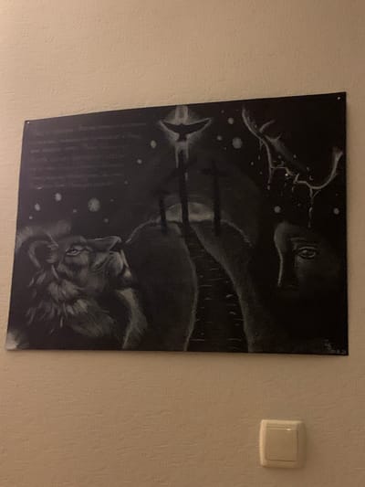 The image shows a black and white painting on a textured, beige wall. The painting is abstract and features a lion's head on the left, looking upwards. In the center, there are three figures with what appear to be halos, standing on a dark, indistinct path. Above them, a bird is silhouetted against a starry sky. On the right side of the painting, there is a profile of a human face, seemingly emerging from a dark, stormy background with lightning. The painting is attached to the wall with what appear to be two small pins or screws at the top. Below the painting, there is a light switch with a white cover. The overall scene appears to be an indoor setting, likely a room in a residential or public building. There is no discernible information in the image that would place it specifically within the Чыжэвіцкі сельскі Савет, Belarus.
