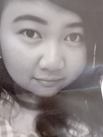 A black and white, close-up portrait features a young East Asian female. Her face occupies the majority of the frame, with her head slightly tilted. She has dark, well-defined eyebrows and dark eyes that gaze directly towards the viewer. A faint, gentle smile is present on her lips. Dark hair frames her face on both sides, though more prominently visible on the left. The background is dark and out of focus, emphasizing her facial features. The image exhibits a grainy or textured quality, consistent with a scanned photograph or a printed document. The lighting is soft and even across her face. Her overall expression is calm and composed. The context provided indicates the location as Kaohsiung, Taiwan. No specific objects or visible text are discernible within the image.