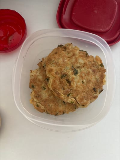The image shows two round, golden-brown patties inside a clear plastic container. Next to the container are two red lids, one square and one round. The patties appear to be food items, possibly crab cakes or veggie burgers. The background is a plain white surface. The image provides no information about the location being in Buenavista, Mexico or any activities taking place.
