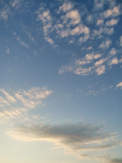 The image captures a vast expanse of sky above the city of Obligado, Paraguay. The sky is a clear, pale blue, transitioning to a lighter hue near the horizon. Scattered across the sky are numerous clouds, varying in size and density. Some clouds are wispy and thin, appearing as delicate brushstrokes against the blue canvas, while others are more pronounced, with soft, rounded edges. The lighting suggests it is either early morning or late afternoon, with a gentle, diffused sunlight illuminating the clouds from the side, giving them a warm, golden glow in some areas. The overall impression is one of tranquility and open space.