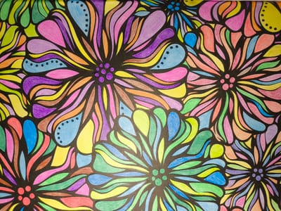 The image is a close-up, overhead shot of a black background filled with a vibrant, abstract floral pattern. The petals of the flowers are rendered in a variety of bright colors, including pink, purple, yellow, orange, blue, and green, outlined in black. Some of the petals have a teardrop or flame-like shape, while others are more elongated and curved. Within some of the blue, teardrop-shaped petals, there are clusters of small black dots. The overall impression is one of a lively and colorful, almost psychedelic, design. There are no people, objects, or environmental elements visible that would indicate a specific location, including the city of Pomezia, Italy.