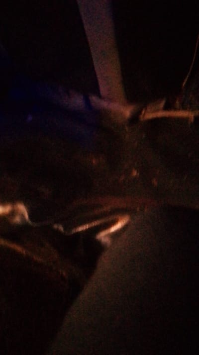 A dark, blurry image presents a limited view. A light-colored, narrow strip appears vertically, possibly a wall or structural element. A dim blue area suggests a light source. Shadowy forms dominate, hinting at shapes such as an unidentified object or furniture in the lower left corner. The overall lack of clarity makes precise identification impossible.