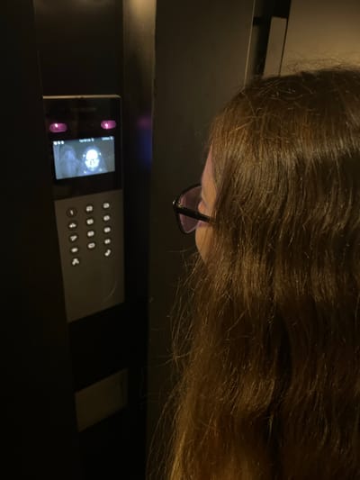 A woman with long, brown hair and eyeglasses is seen looking at a black Nesa V-Home control panel with a screen and keypad. The environment appears to be indoors with dark surroundings. There is no evidence in the image to suggest the location is in Bahía Blanca, Argentina.