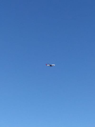 An airplane, identified by its red and white tail, is visible flying in a clear blue sky. The airplane appears to be a commercial jetliner. The image does not contain any elements that would allow for a specific location within Bischofsheim, Germany, to be identified. The environment is solely the sky.