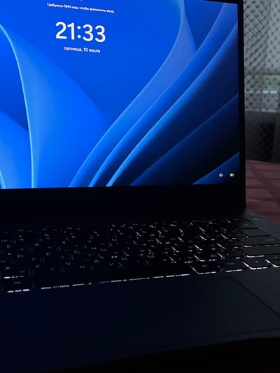 The image displays a close-up of a laptop screen showing a lock screen with the time "21:33" and the date "пятница, 10 июля" (Friday, July 10). The background is a blue abstract design. The text above the time reads "Требуется ПИН-код, чтобы выполнить вход." (PIN code required to log in.). The Huawei logo is visible on the laptop's bezel. The keyboard is illuminated. The scene is likely indoors, given the illuminated keyboard and the absence of natural light suggesting it's nighttime or a dark room. The location of Linyovo, Russia, is not indicated by any visual cues in the image itself.