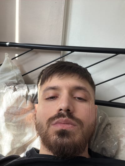 A man with dark hair and a beard lies on a white pillow in a bed with a black metal frame. The room appears to have white walls. The location cannot be determined as Pentre, United Kingdom without further information.