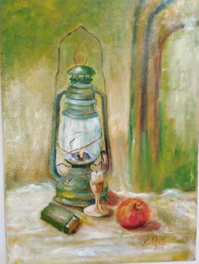 This is an oil painting on canvas depicting a still life. The primary subject is a green kerosene lantern, lit and casting a warm glow from within. The lantern sits on a surface that appears to be a table or cloth, rendered in muted, textured colors. To the left of the lantern is a small, rectangular green object, likely a box of matches. To the right of the lantern, a single red fruit, possibly an apple or pomegranate, rests on the surface. Behind the objects, the background is painted in soft, impressionistic strokes of green and yellow, suggesting an outdoor setting or a room with soft lighting. A hint of architectural detail, possibly an archway or window frame, is visible in the upper right portion of the painting. The overall mood is tranquil and perhaps nostalgic, with the lit lantern evoking a sense of warmth and a bygone era. The artist's signature, "J. Iladi," and the year "2017" are visible in the lower right corner of the painting. The context of Pardes Hana-Karkur, Israel, suggests the setting might be a home or a quaint outdoor space within that region.