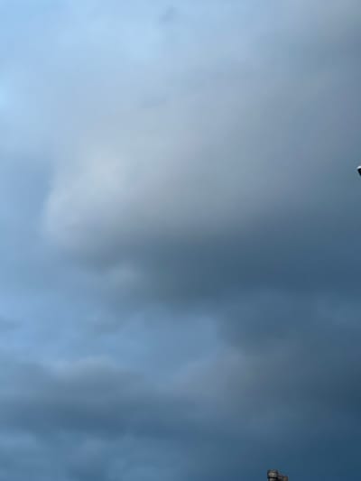 The image shows a cloudy sky over Stoke-on-Trent, United Kingdom. The clouds are dark and appear to be gathering, suggesting a change in weather. In the lower right corner of the image, a small portion of a building with turrets is visible, possibly part of a historical structure. The overall impression is one of an overcast day in an urban environment.