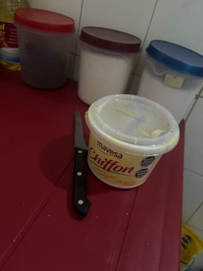 The image shows a red table with three plastic containers with lids of different colors (blue, red, and maroon), a container of Mavesa Chiffon margarine with a white lid, and a knife with a black handle. The location, San Juan de Los Morros, Venezuela, cannot be confirmed from the image.