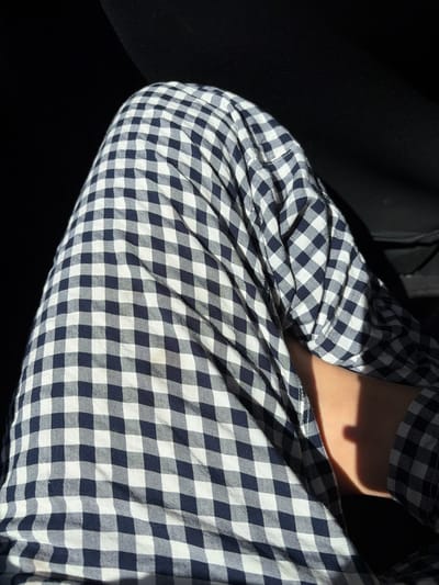 A person wearing a blue and white gingham-patterned long-sleeved shirt is depicted close-up. The sleeve of the shirt is pushed up, revealing a small portion of the wearer's arm, brightly lit. The shirt material is bunched up with numerous folds and creases. The left side of the image is dark, providing a strong contrast with the illuminated fabric and skin.