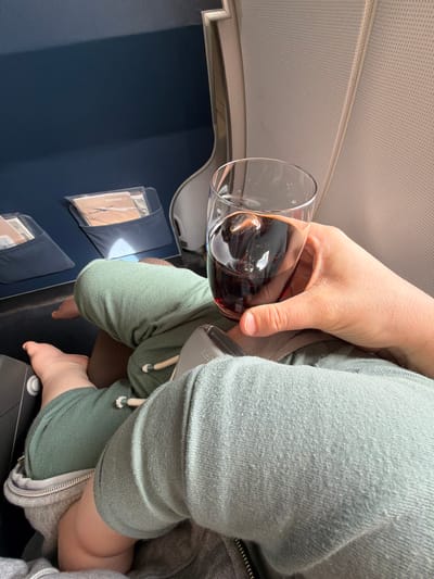 A person is holding a glass of red wine on an airplane. A child is sitting on the person's lap. The interior of the airplane cabin is visible. There is no indication the scene is located in Walldorf, Germany.