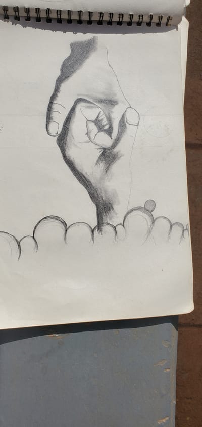 A pencil sketch on a spiral-bound notepad depicts a hand with fingers curled into a fist. The sketch is of a light gray notepad with a black spiral binding at the top. The notepad is open and lies on a surface that appears to be a gray table or bench. The drawing shows shading to create depth and form on the hand. The bottom of the sketch features a row of overlapping circles, possibly representing bubbles or a decorative element. The sketch is oriented vertically, with the top of the notepad at the top of the image. The background of the sketch is a plain white page. The notepad itself appears to be aged, with some slight discoloration. The scene is set outdoors, as evidenced by the brown brick-like texture visible in the top right corner, suggesting an outdoor setting in or around Goni Gara, Nigeria.