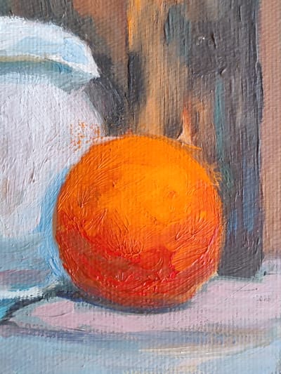 The image is a close-up, cropped view of an oil painting. The dominant subject is a round, vibrant orange fruit, likely an orange or tangerine, rendered with thick, textured brushstrokes that create a palpable surface. The fruit is positioned on a surface with hints of pink and blue. To the left of the fruit, a portion of a white, jug-like object with blue and grey accents is visible, also painted with textured strokes. In the background, vertical lines of dark gray, brown, and orange suggest a wooden surface or a backdrop. The lighting appears to be from the right, casting subtle shadows and highlighting the textured impasto of the paint. The painting has a still life quality, focusing on the texture and color of the depicted objects. The image does not contain any information about the city of Rybnitsa, Moldova.
